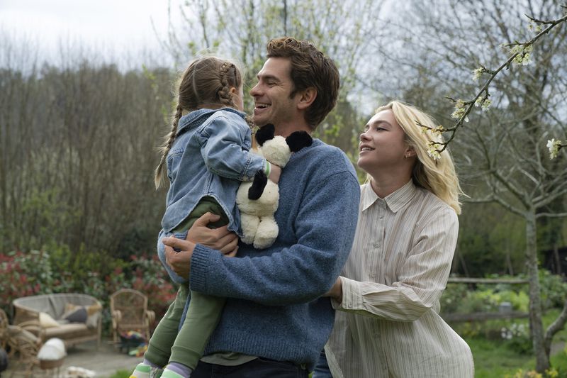 This image released by A24 shows Andrew Garfield, center, and Florence Pugh, right, in a scene from "We Live In Time." (Peter Mountain/A24 via AP)