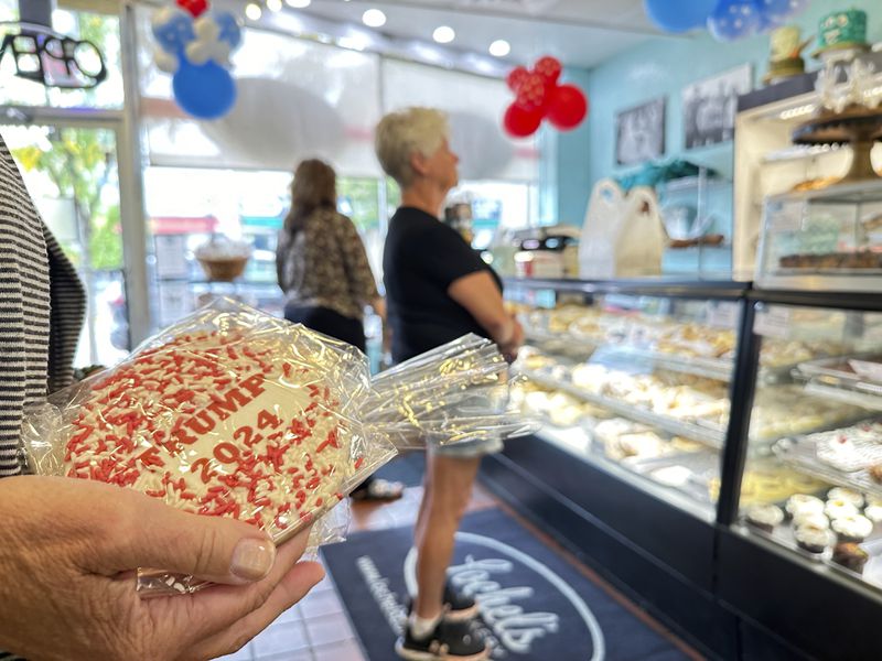 A customer holds a sugar cookie with a Trump 2024 label on at Lochel's Bakery in the town of Hatboro in suburban Philadelphia, Tuesday, Sept. 24, 2024. Lochel's Bakery started the election cookie poll in 2008 as a joke between the third-generation bakery owners and their local customers. (AP Photo/Tassanee Vejpongsa)