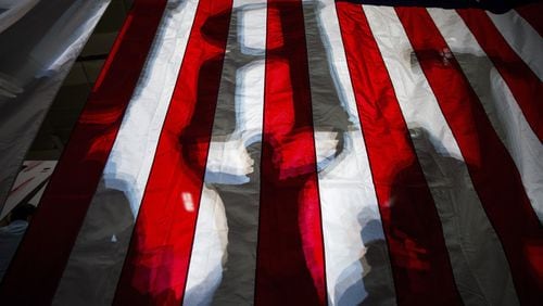 Shadows of Donald Trump supporters, holding up letters to spell his name, show through an American flag at a campaign event for the Republican presidential nominee, at the Travis County Exposition Center in Austin, Texas, Aug. 23, 2016. On Thursday, Hillary Clinton plans to delivered a major address denouncing Trump’s embrace of the “alt-right” political philosophy, presenting his choice as an especially ominous turn in a presidential election full of them. (Damon Winter/The New York Times)