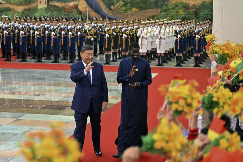 In this photo released by Xinhua News Agency, visiting Senegal's President Bassirou Diomaye Faye, right, and Chinese President Xi Jinping gesture as they are greeted by children waving flowers and flags during a welcome ceremony at the Great Hall of the People in Beijing, Wednesday, Sept. 4, 2024, ahead of the China Africa Forum. (Yin Bogu/Xinhua via AP)