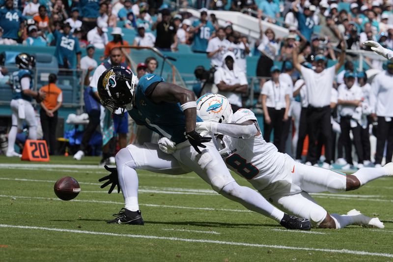 Miami Dolphins safety Jevon Holland (8) grabs Jacksonville Jaguars running back Travis Etienne Jr. (1) as he fumbles the ball during the second half of an NFL football game, Sunday, Sept. 8, 2024, in Miami Gardens, Fla. (AP Photo/Rebecca Blackwell)