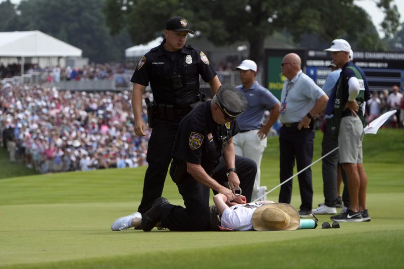 A protester is taken into custody after they ran onto the course as Tom Kim, center, of South Korea, watches on the 18th hole during the final round of the Travelers Championship golf tournament at TPC River Highlands, Sunday, June 23, 2024, in Cromwell, Conn. (AP Photo/Seth Wenig)