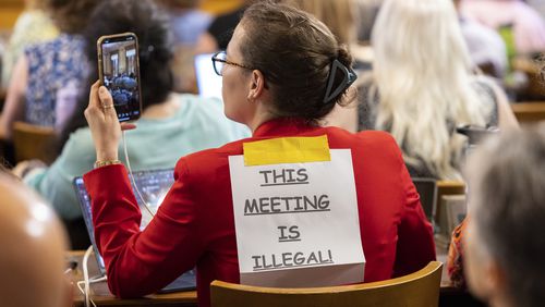 Marisa Pyle, a lobbyist with All Voting is Local, wears a sign that says "This Meeting is Illegal" during a hastily planned July 12 State Election Board meeting at the Capitol in Atlanta. (Arvin Temkar/Atlanta Journal-Constitution)