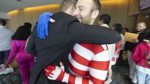 Jima Parkis, dressed in an American flag, hugs his friend James Watson, who emigrated from England, after the Naturalization Ceremony for 150 new citizens in the Gwinnett Justice and Administration Center auditorium Tuesday July 2 2024. (Steve Schaefer / AJC)