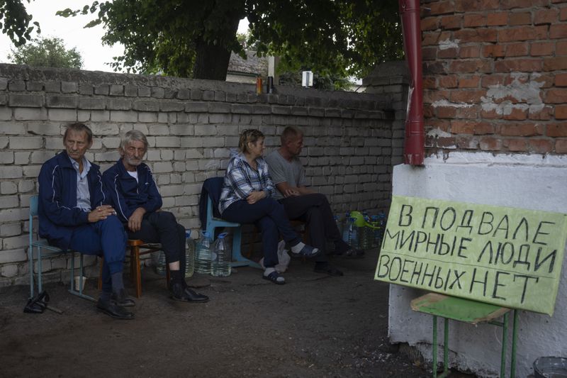 Local residents sit near a shelter in Sudzha, Kursk region, Russia, Friday, Aug. 16, 2024. The sign reads “Civilians in a basement. No military.” This image was approved by the Ukrainian Defense Ministry before publication. (AP Photo)