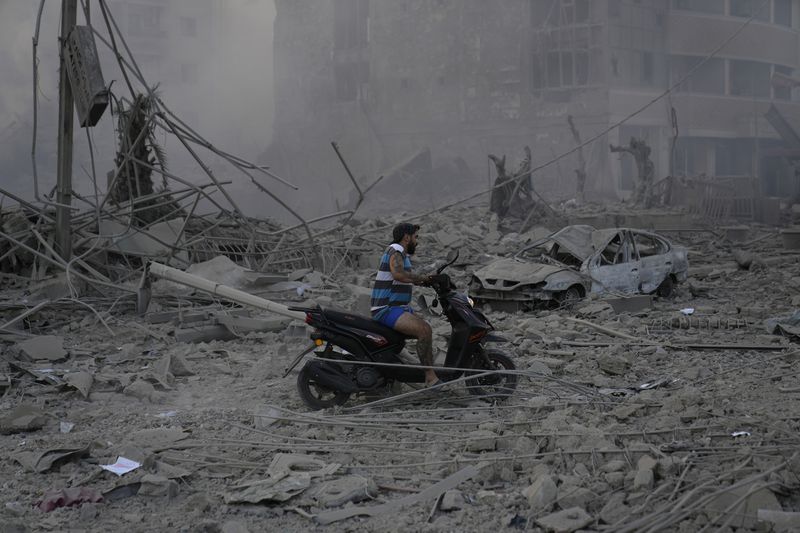 A man rides his scooter as he drives on the debris of destroyed buildings that were hit by Israeli airstrikes in Dahiyeh, Beirut, Lebanon, Sunday, Oct. 6, 2024. (AP Photo/Hussein Malla)