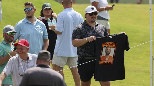 A golf fan holds up a “Free Scottie,” t-shirt as Scottie Scheffler walks by after his tee shot on the 18th hole during a practice round for the Tour Championship at East Lake Golf Club, on Wednesday, Aug. 28, 2024, in Atlanta. (Jason Getz / AJC)
