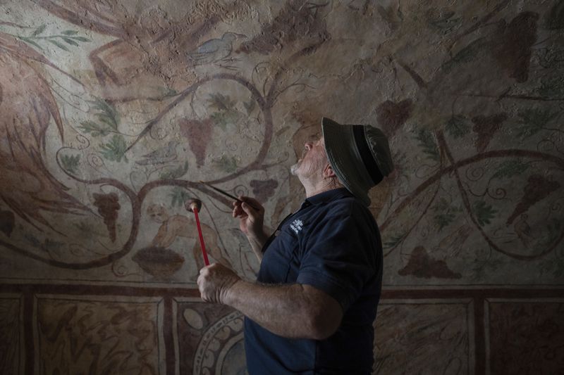 A worker touches up an ancient wall of the archeological tomb site in Ashkelon, Israel, Tuesday, Aug. 27, 2024. The tomb with wall paintings depicting Greek mythological figures is at least 1,700 years old said the Israeli Antiquities Authority, whose workers are restoring the site. (AP Photo/Ohad Zwigenberg)