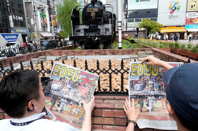 Pedestrians read an extra edition of the Sports Nippon newspaper reporting on the Los Angeles Dodgers' Shohei Ohtani becoming the first player in major league history with 50 home runs and 50 stolen bases in a season, Friday, Sept. 20, 2024, in Tokyo. (AP Photo/Eugene Hoshiko)