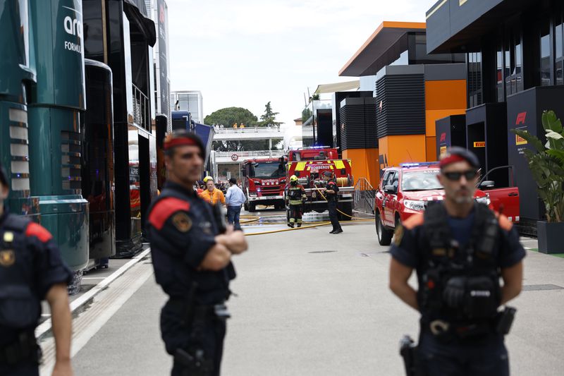 Police and firefighters stand in the paddock after the McLaren F1 team were forced to evacuate its hospitality suite due to a fire during the 3rd practice session for the Formula 1 Spanish Grand Prix at the Barcelona Catalunya racetrack in Montmelo, near Barcelona, Spain, Saturday, June 22, 2024. The British team says there were no injuries. (AP Photo/Joan Monfort)
