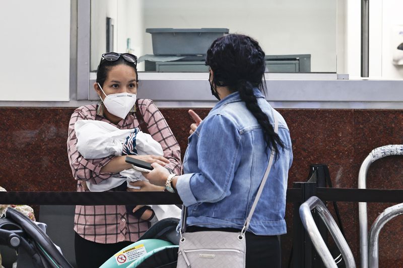 Yariela Riviera (left) from Honduras holds her baby while talking to Marimet Pacheco (right) at Hartsfield-Jackson International Airport on Tuesday, July 19, 2022. She says she still wears her mask to stay safe and to prevent herself from getting Covid-19. (Natrice Miller/natrice.miller@ajc.com)