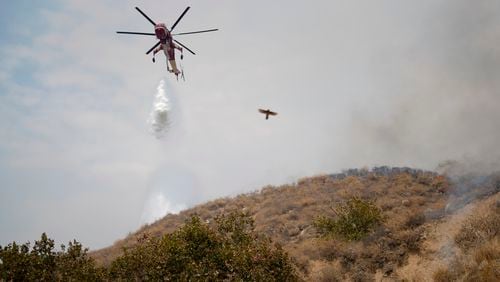 A helicopter drops water onto the Line Fire Saturday, Sept. 7, 2024, in Highland, Calif. (AP Photo/Eric Thayer)