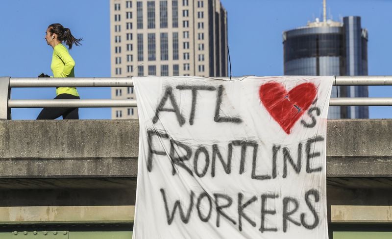 Since the start of the pandemic, tensions have mounted between frontline healthcare workers and their employers, as hospitals have ordered doctors and nurses to work around a deadly contagion while conserving personal protective equipment. Pictured here, a shout-out to frontline workers is expressed by a banner hanging from the Jackson Street Bridge, visible to westbound motorists on John Lewis Freedom Parkway. JOHN SPINK/JSPINK@AJC.COM