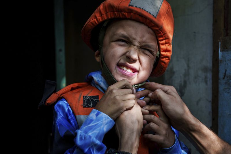 A Fenix team rescue worker places a helmet on Bohdan Scherbyna, 9, as he is evacuated with his mother Maryna Scherbyna and 14 year old sister Angelina Scherbyna, as local people as moved from Selidove to safe areas, in Pokrovsk, Donetsk region, Ukraine, on Tuesday, Aug. 20, 2024. (AP Photo/Evgeniy Maloletka)