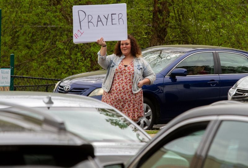Summer Osbon holds up a sign as her father, Pastor Shell Osbon, talks to the crowd during the Drive-in church service at the Life Church Smyrna Assembly of God Sunday, April 5, 2020 STEVE SCHAEFER / SPECIAL TO THE AJC