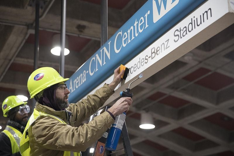 01/16/2019 — Atlanta, Georgia — Tim Carl (second from left) of Advantage Graphics & Signs uses a torch to gaurantee the cohesiveness of the new Mercedes-Benz signage at the MARTA Dome/GWCC/Philips Arena/CNN Center Transit in Atlanta, Wednesday, January 16, 2019. Advantage Graphics & Signs worked in the transit station on Wednesday to replace signage that mislabeled Atlanta’s two newly named sport stadiums. (ALYSSA POINTER/ALYSSA.POINTER@AJC.COM)