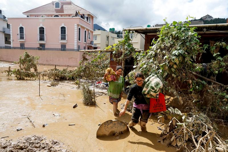 Women walk with their belongings in the mud in Kathmandu, Nepal, Monday, Sept. 30, 2024 in the aftermath of a flood caused by heavy rains. (AP Photo/Gopen Rai)