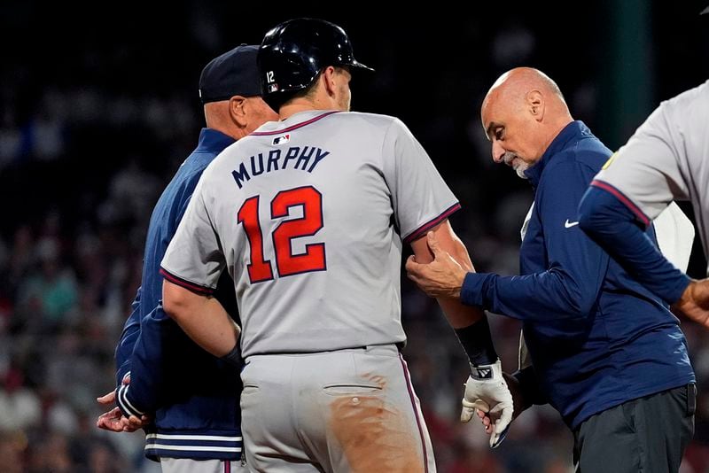 Atlanta Braves' Sean Murphy (12) has his right elbow examined by trainer George Poulis after getting hit by a pitch by Boston Red Sox's Chase Anderson during the ninth inning of a baseball game Tuesday, June 4, 2024, at Fenway Park in Boston. (AP Photo/Charles Krupa)