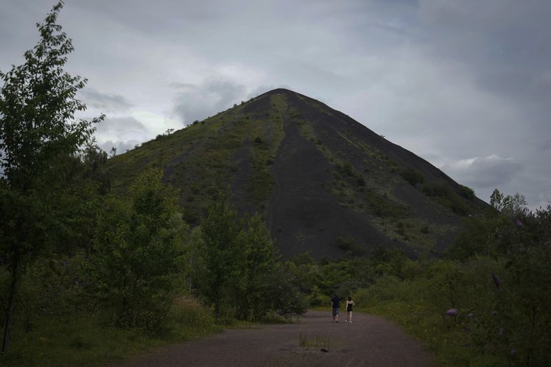 People stroll by the Saint Henriette slag heap in Henin-Beaumont, northern France, Sunday, June 30, 2024. Several waves of industrial shutdowns have left unemployment levels above the national average, and 60% of the population earns so little it does not need to pay tax, according to data from France's national statistics agency. (AP Photo/Thibault Camus, File)