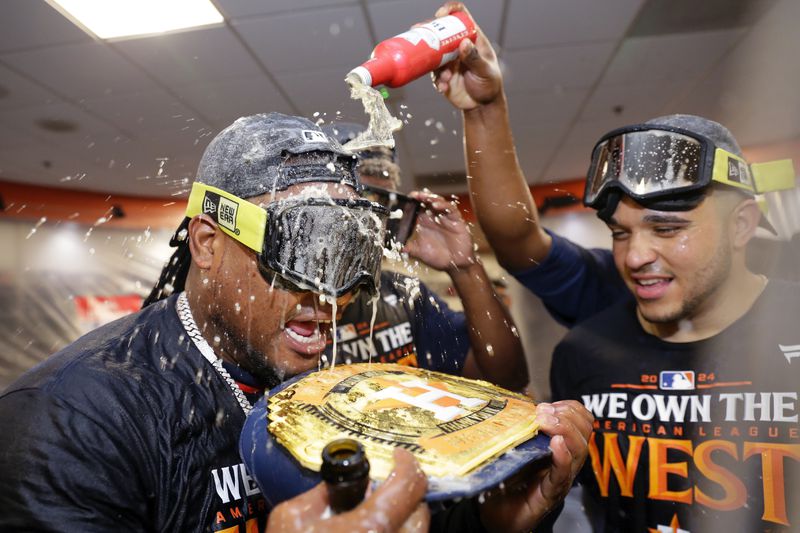 Houston Astros starting pitcher Framber Valdez, left, holds an Astros title belt as he is doused with beer next to Yainer Diaz, right, as the team celebrates in the clubhouse after defeating the Seattle Mariners 4-3 to clinch the AL West title after a baseball game Tuesday, Sept. 24, 2024, in Houston. (AP Photo/Michael Wyke)