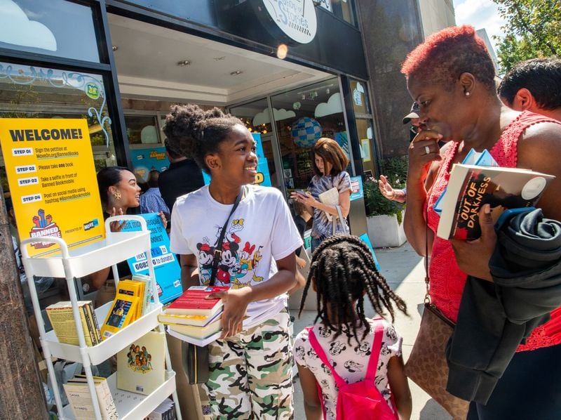 MoveOn Political Action's Banned Bookmobile is distributing free banned books at the kickoff of National Banned Book Week where Kimora Bernard, 12, from left, her sister, Kimiyah, 5, and grandmother Carmen Bernard, right, of Stone Mountain, pick out a few of the banned books that cannot be checked out at public school libraries Sunday, Oct 1, 2023 at Little Shop of Stories in Decatur Square.  (Jenni Girtman for The Atlanta Journal-Constitution)