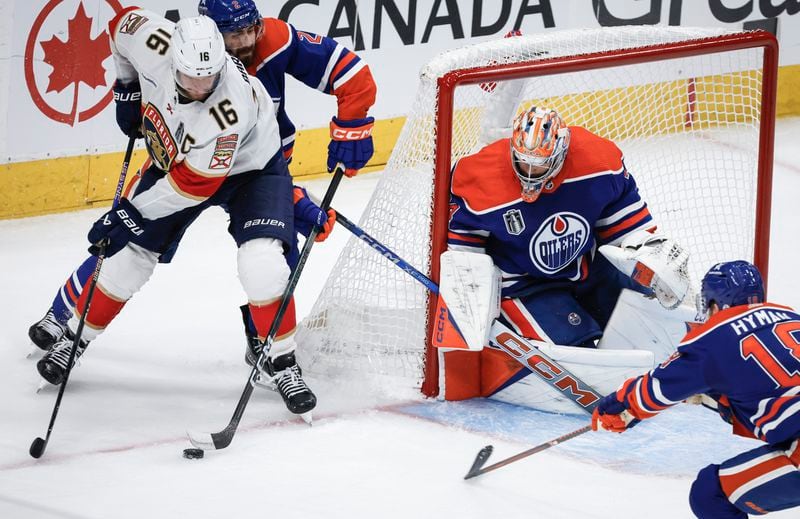 Florida Panthers' Aleksander Barkov (16) tries to get the puck as he is is checked by Edmonton Oilers' Evan Bouchard (2) while goalie Stuart Skinner (74) guards the net during the third period of Game 4 of the NHL hockey Stanley Cup Final, Saturday, June 15, 2024, in Edmonton, Alberta. (Jeff McIntosh/The Canadian Press via AP)