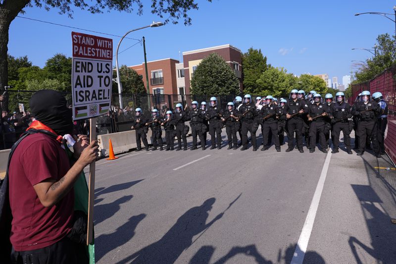 Police walk towards protesters who knock down a fence surrounding United Center at the Democratic National Convention after a march Monday, Aug. 19, 2024, in Chicago. (AP Photo/Alex Brandon)