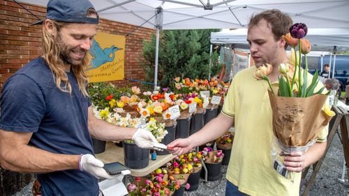 Evan Neal (L) takes a payment for flowers from Walker Loucks at the Grant Park Farmers Market Sunday, March 29, 2020. STEVE SCHAEFER / SPECIAL TO THE AJC
