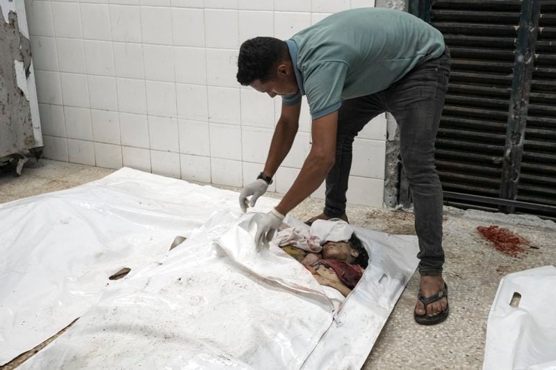 EDS NOTE: GRAPHIC CONTENT - A worker unzips a body bag to display a Palestinian family, consisting of five children aged 2 to 11 and their parents, in the morgue at Al-Aqsa Martyrs Hospital in Deir al-Balah, Gaza Strip, after an Israeli strike hit their home in the Nuseirat refugee camp, Wednesday, Aug. 14, 2024. (AP Photo/Abdel Kareem Hana)