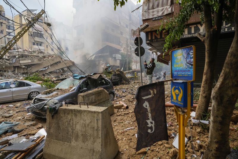 A man documents the damaged buildings at the site of an Israeli airstrike in Beirut's southern suburb, Lebanon, Tuesday, Oct. 1, 2024. (AP Photo/Hassan Ammar)