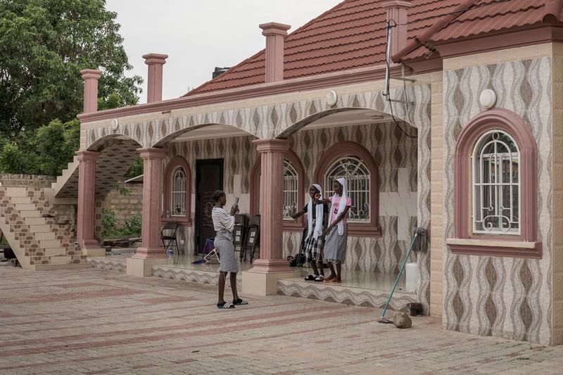 Teenagers record a TikTok video on the steps of a house owned by a migrant living in Seattle, U.S., in the village of Kaiaf, Gambia, on July 27, 2024. (AP Photo/Annika Hammerschlag)