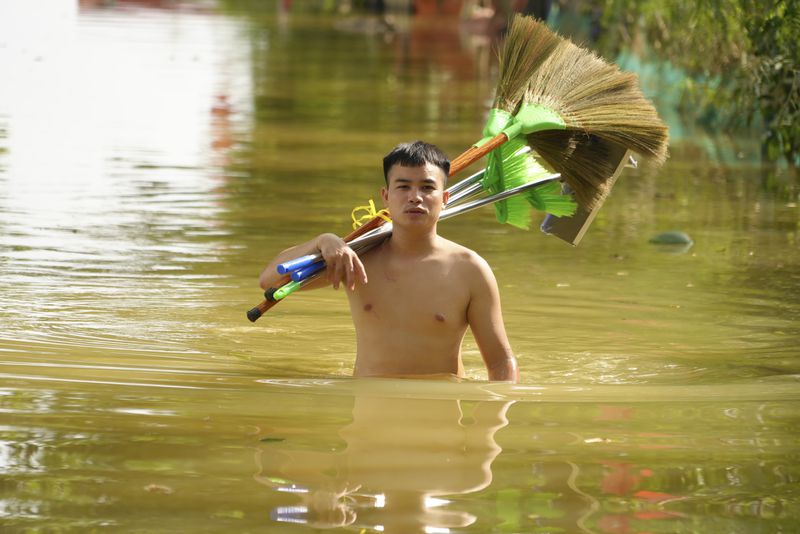 A man wades in flood carrying brooms to clean up houses as flood starts to recede in the aftermath of Typhoon Yagi in An Lac village, Hanoi, Vietnam Friday, Sept. 13, 2024. (AP Photo/Hau Dinh)