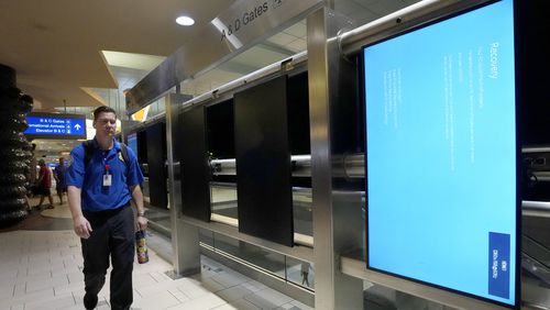 An employee walks past rebooting arrivals and departures screens at Phoenix Sky Harbor International Airport Friday, July 19, 2024, in Phoenix. An overnight outage was blamed on a software update that cybersecurity firm CrowdStrike sent to Microsoft computers of its corporate customers including many airlines. (AP Photo/Ross D. Franklin)