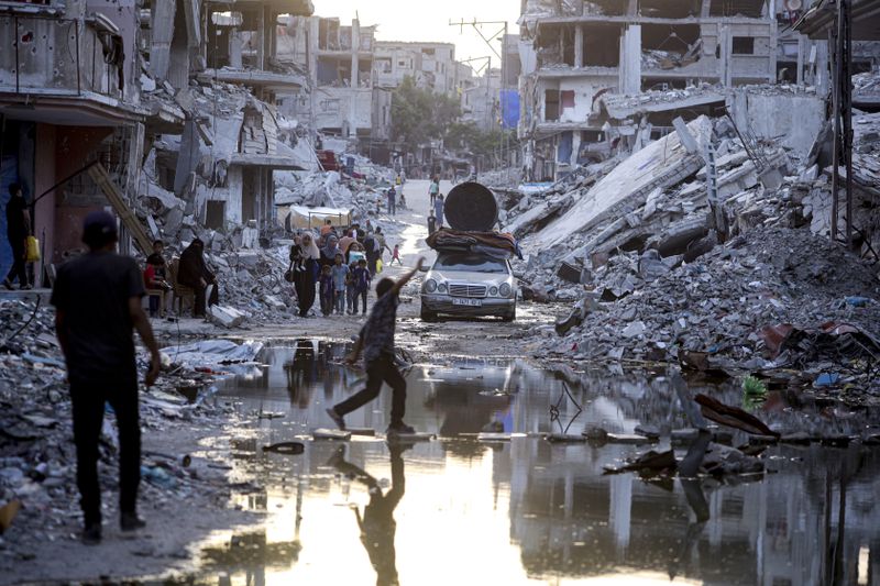 FILE - Palestinians displaced by the Israeli air and ground offensive on the Gaza Strip, walk past sewage flowing into the streets of the southern town of Khan Younis, Gaza Strip, Thursday, July 4, 2024. Health authorities and aid agencies are racing to avert an outbreak of polio in the Gaza Strip after the virus was detected in the territory's wastewater and three cases with a suspected polio symptom have been reported. (AP Photo/Jehad Alshrafi, File)