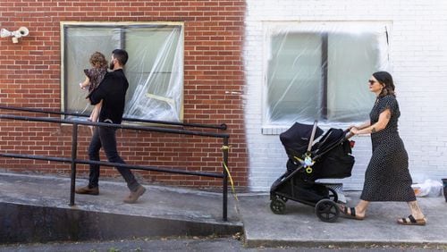 (L-R) Tyler Smith, holding Lennon, 2, and Grace Smith, pushing River, 5 months, walk into the building that will house their new bookstore in Chamblee on Friday, May 31, 2024. (Arvin Temkar / AJC)