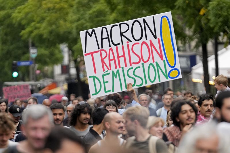 A demonstrator holds a poster which reads 'Macron treason resignation' during a protest, responding to a call from the far-left party who criticized as a power grab the president's appointment of a conservative new prime minister, Michel Barnier, in Paris, France, Saturday, Sept. 7, 2024. (AP Photo/Michel Euler)