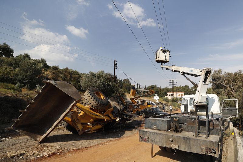 Syrian workers stand on a crane next of a flipped bulldozer in the town of Masyaf, Syria, Monday, Sept. 9, 2024. Syrian state news agency SANA says that Israeli strikes hit several areas in central Syria Sunday night, damaging a highway in Hama province and sparking fires. (AP Photo/Omar Sanadiki)