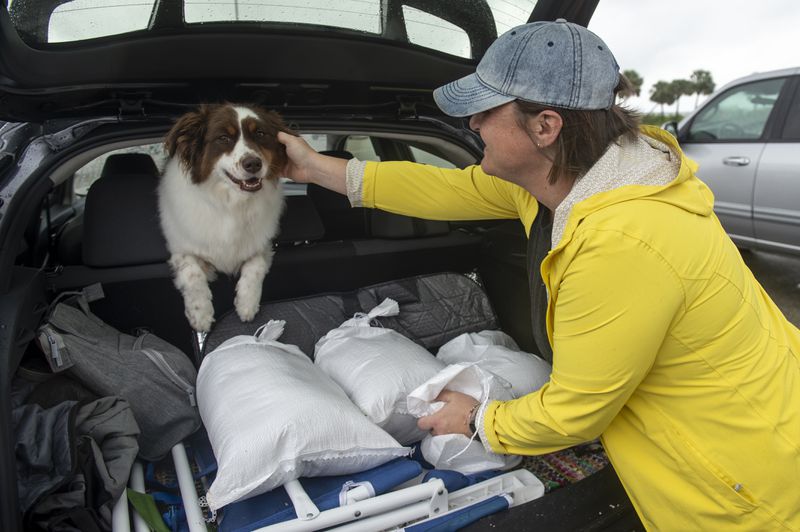 Lindsey Ranney and her dog Fig fill the trunk of Ranney's car with sandbags in preparation for Hurricane Francine from a pile of sand provided by Harrison County at the end of Courthouse Boulevard in Gulfport, Miss. on Tuesday, Sept. 10, 2024. (Hannah Ruhoff/The Sun Herald via AP)