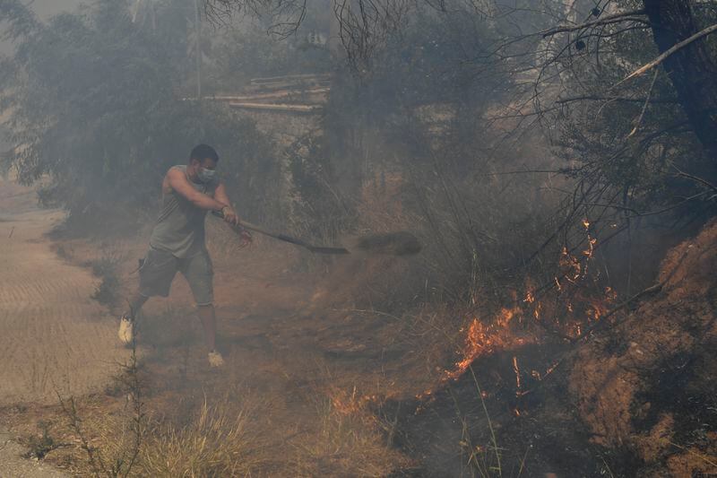 A volunteer throws dirt with a shovel on flames, in Dioni, northeast of Athens, Greece, Monday, Aug. 12, 2024. Hundreds of firefighters backed by dozens of water-dropping planes and helicopters were battling the flames from first light Monday, with a major forest fire that began the previous day raging out of control on the fringes of Athens, fanned by strong winds. (AP Photo/Michael Varaklas)