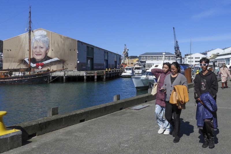 People walk on the waterfront near a mural honoring Maori leader Whae June Te Raumange Jackson as New Zealand celebrates its annual Maori language week in Wellington, New Zealand, Wednesday, Sept. 18, 2024. (AP Photo/Charlotte GrahamMcLay)