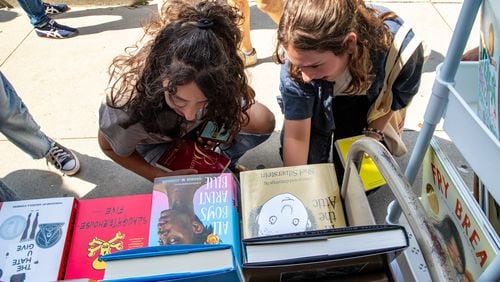 MoveOn Political Action's Banned Bookmobile distributes free banned books at the kickoff of National Banned Book Week where Shereen Mendelson (left) and Isabella Lipham take a look at a few of the banned books that cannot be checked out at public school libraries on Oct. 1, 2023, at Little Shop of Stories in Decatur Square. (Jenni Girtman for the AJC)