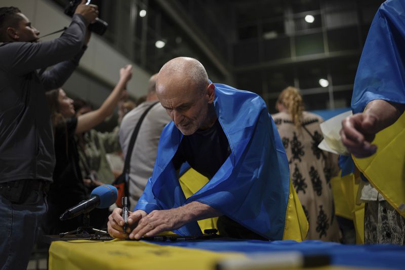 Valeriy Matiushenko, who spent over seven years in Russian captivity, signs the Ukrainian national flag in Kyiv airport, Ukraine, Saturday, June 29, 2024. Ten Ukrainians who had been held prisoners for years, were released from Russian captivity on Friday with a mediation of Vatican, said Ukraine's President Volodymyr Zelenskyy. (AP Photo/Alex Babenko)