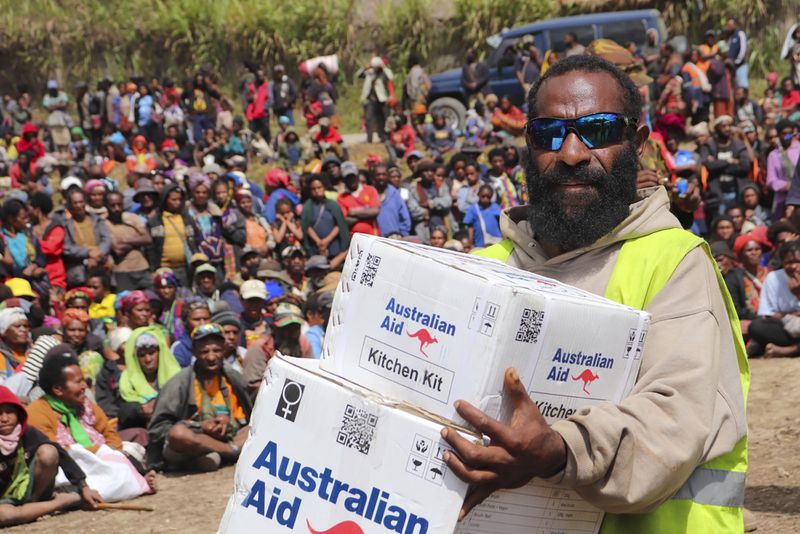 In this photo released by IOM- PNG- A local villager carries boxes of Australian aide at the sight of the landslide at Yambali village in the Papua New Guinea highlands Thursday, June 20, 2024. Australia will provide a further $1.3 million to support reconstruction efforts in Papua New Guinea after last month's deadly landslide. The South Pacific island nation off Australia's northern coast is still struggling with the aftermath of the disaster in Enga province in its mountainous interior. (David Kuna/IOM - PNG via AP)
