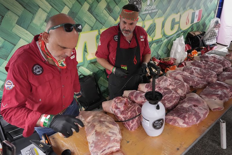 Juan Garza, left, and Mario Villarreal of the Sociedad Mexicano de Parrillieros team season pork shoulders at the World Championship Barbecue Cooking Contest, Friday, May 17, 2024, in Memphis, Tenn. (AP Photo/George Walker IV)