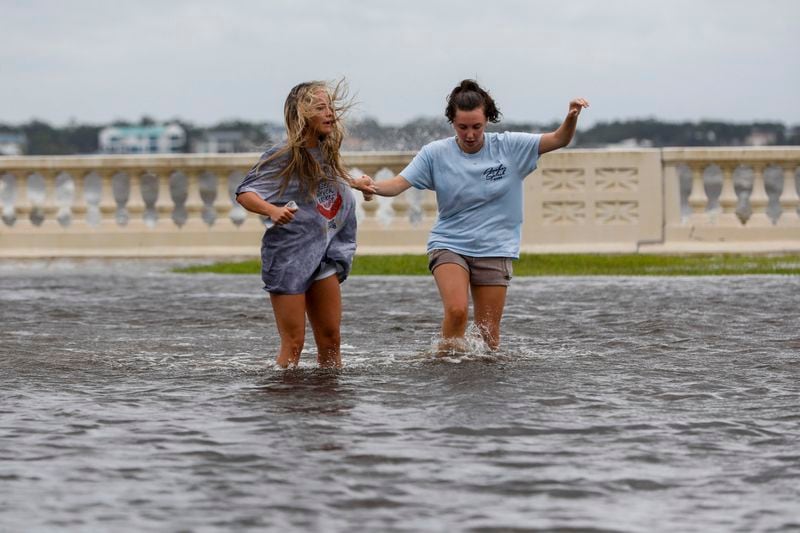 Camryn Frick, left, and Jillian Sternick, both 22, and of Tampa, hold hands as they cross a flooded street together along Bayshore Boulevard on Thursday, Sept. 26, 2024, in Tampa, Fla. (Jefferee Woo/Tampa Bay Times via AP)