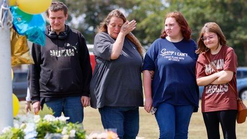 April Johnson, second from left, pays her respects at the Apalachee High School flag pole the day after a four people died in a shooting. She's pictured here with her son Gavin, left, daughter Jasmine, second from right, and Hanna Thompson, right, on Thursday, Sept. 5, 2024. April and Jasmine were texting each other during and after the shooting before the family was able to reunite. (Miguel Martinez/AJC)