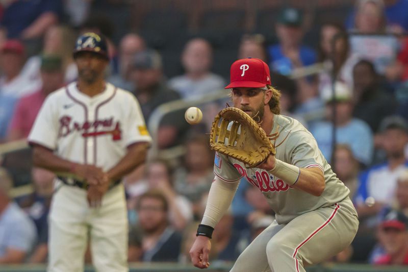 Philadelphia Phillies first baseman Bryce Harper catches a throw from third baseman Alec Bohm (28) before Atlanta Braves' Whit Merrifield (15) can reach first base in the third inning of a baseball game, Wednesday, Aug. 21, 2024, in Atlanta. (AP Photo/Jason Allen)