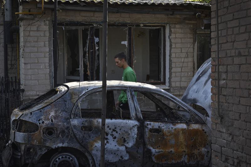 A man passes by a damaged car after a Russian rocket attack in Malokaterynivka, Zaporizhzhia region, Ukraine, Wednesday, Aug. 21, 2024. (AP Photo/Andriy Andriyenko)