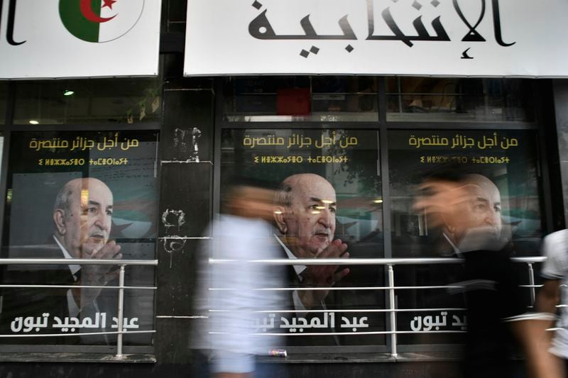 People walk past posters of Algerian President Abdelmadjid Tebboune, after the presidential election results were announced, Sunday, Sept. 8, 2024, in the capital Algiers. (AP Photo/Fateh Guidoum)