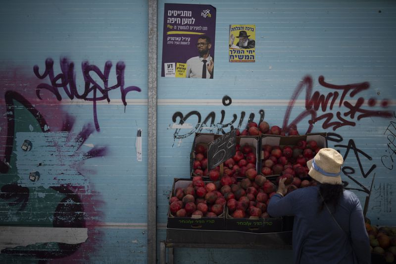 A woman checks the pomegranates displayed at a street market in Haifa, Israel, Friday, Aug. 16, 2024. Israel's economy is suffering from the nearly 11-month war with Hamas, as its leaders grind ahead with its offensive in Gaza that threatens to escalate into a wider conflict. (AP Photo/Leo Correa)